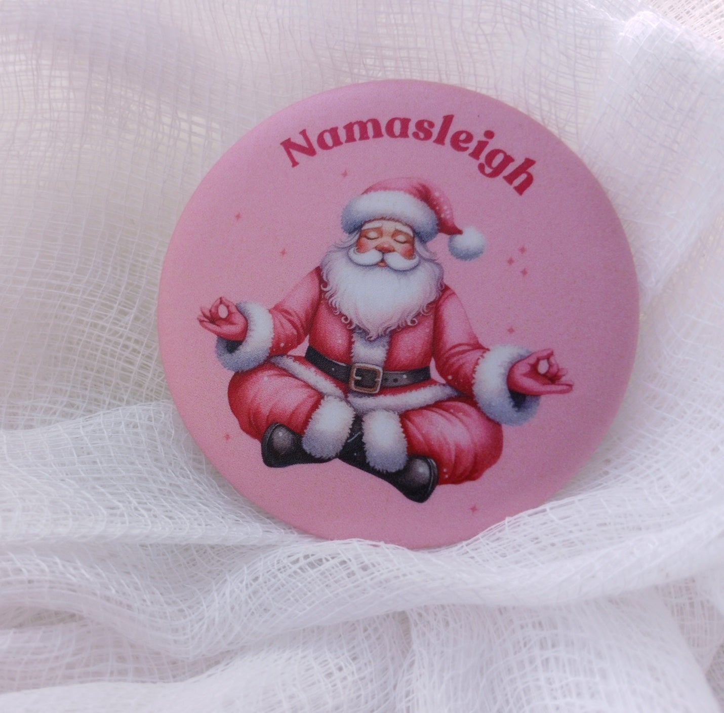 Pink Santa doing a yoga pose with stars around him. The quote above him reads Namasleigh on a magnet or button.